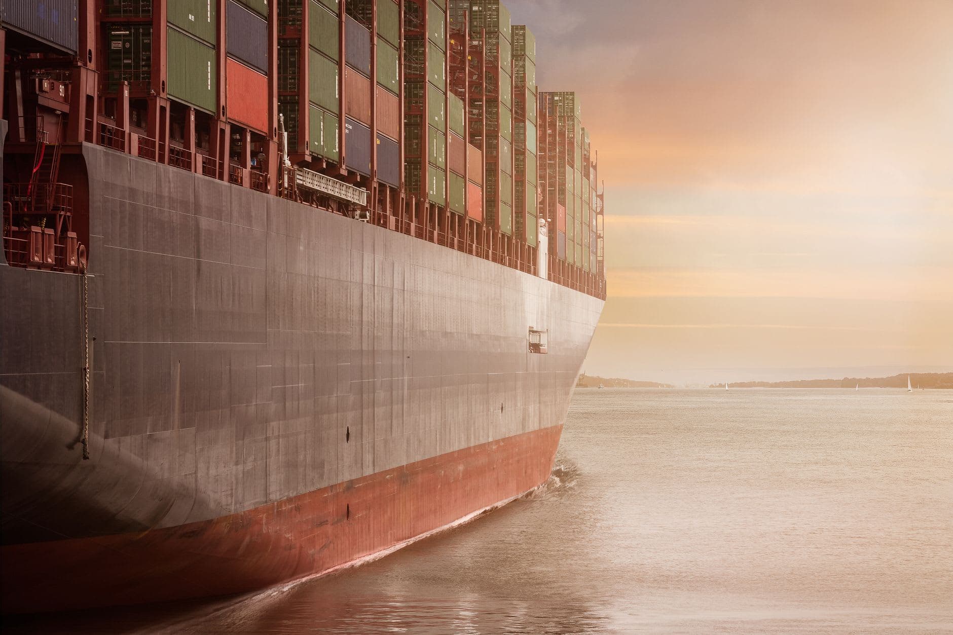 A fully laden container ship under way at dusk, seen close along its hull